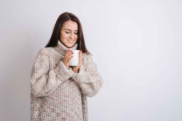 Menina animada, desfrutando de chá quente, vestindo blusa quente em fundo cinza