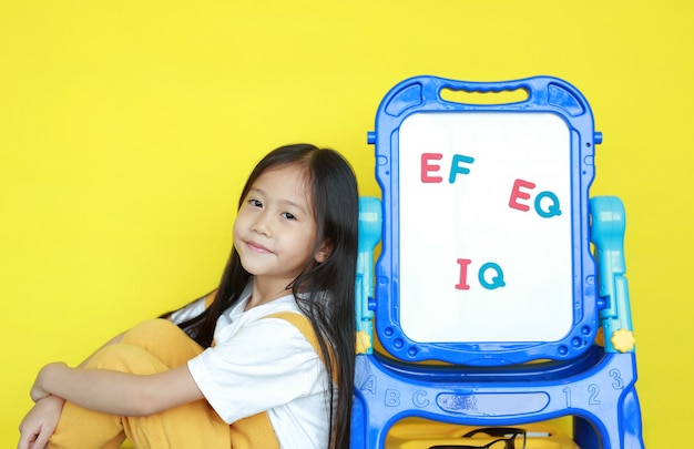 Menina ao lado do quadro branco sobre fundo amarelo