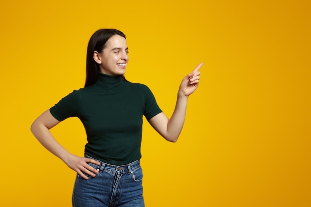 Foto menina apontando os dedos para o espaço da cópia em pé contra um fundo amarelo conceito de publicidade