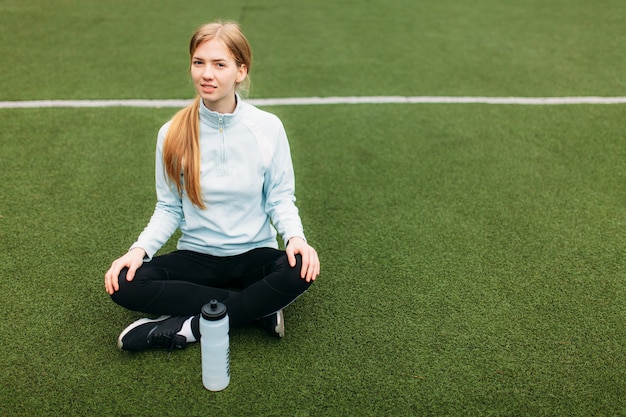 Menina após o exercício, água potável no campo de futebol. Retrato de uma menina bonita no sportswear.