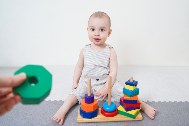 Menina aprende a montar uma pirâmide. desenvolvimento precoce de crianças até um ano de idade. criança morde um brinquedo