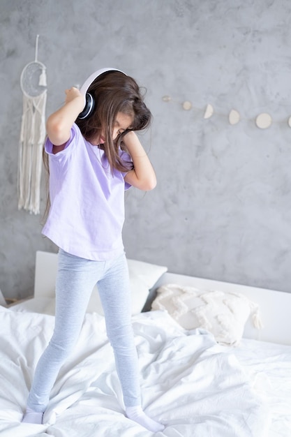 Foto menina árabe bonita com cabelo comprido no fone de ouvido sem fio ouvindo música dançando na cama em casa