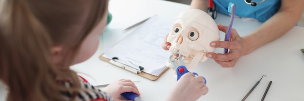 Menina arrancando dente com instrumentos médicos de brinquedo no crânio astronômico no dentista ...