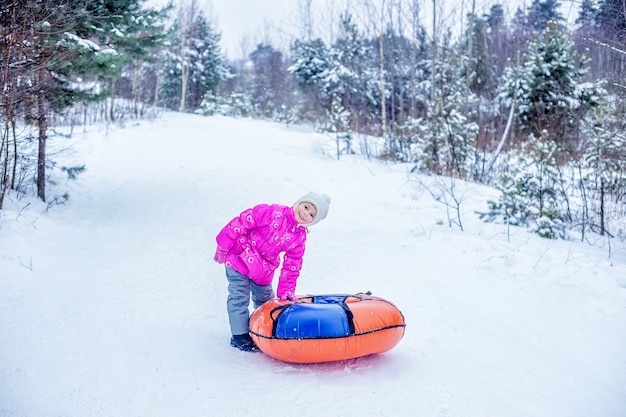 Menina arrasta cheesecake de slide-slide colina nevada. Conceito de atividades ao ar livre de inverno para crianças.