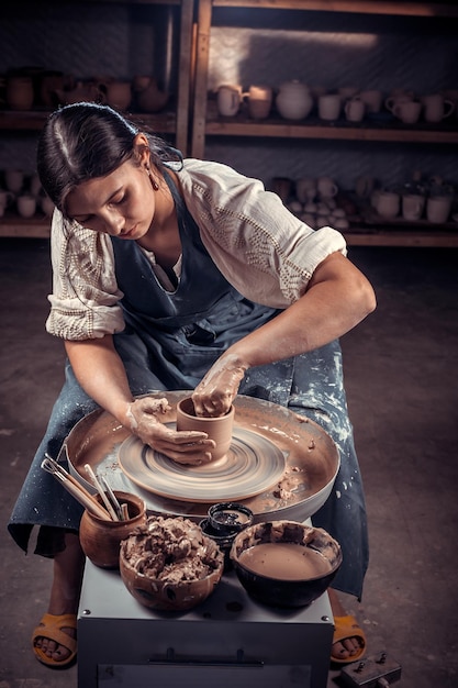 Foto menina artesã elegante demonstra o processo de fabricação de pratos de cerâmica usando a tecnologia antiga. produção de artesanato.