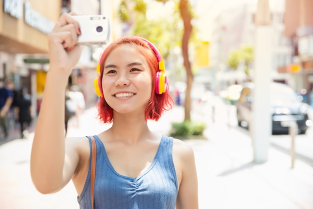 Menina asiática adolescente feliz sorrindo para viajar com a câmera e tirar uma foto ao ar livre da cidade, temporada de verão