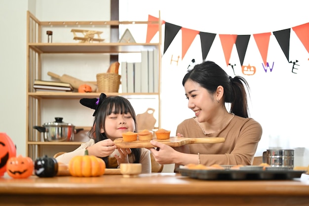 Menina asiática alegre assando cupcakes de Halloween e cheirando cupcakes gostosos família feliz