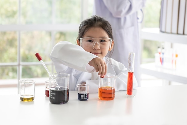 Menina asiática aprendendo e realizou um experimento científico com um copo de medição e um tubo de ensaio colocado