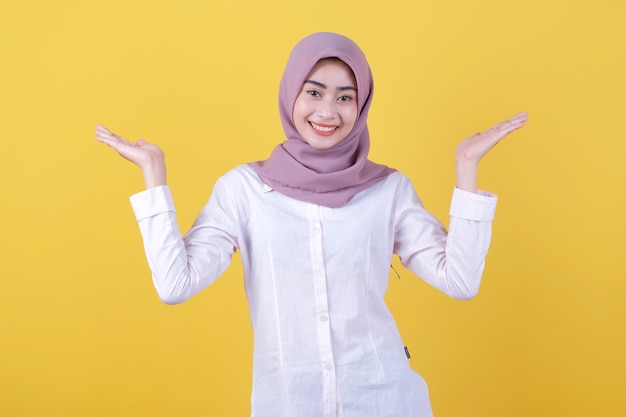 Menina asiática atraente mostrando algo em mãos usando hijab