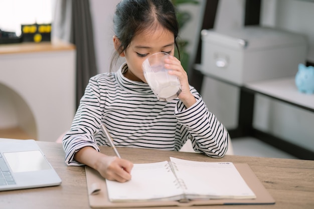 Menina asiática bonita bebendo leite na mesa em casa gosta de beber leite