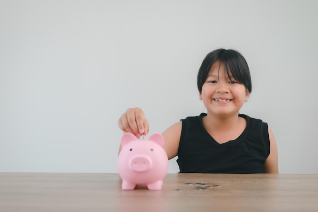 Menina asiática bonita colocando dinheiro no cofrinho para economizar dinheiro para o futuro