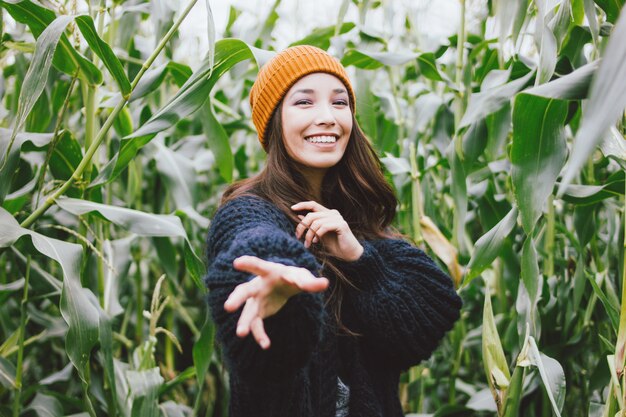 Menina asiática bonita que veste o chapéu amarelo e a camisola feita malha no campo de milho do outono.