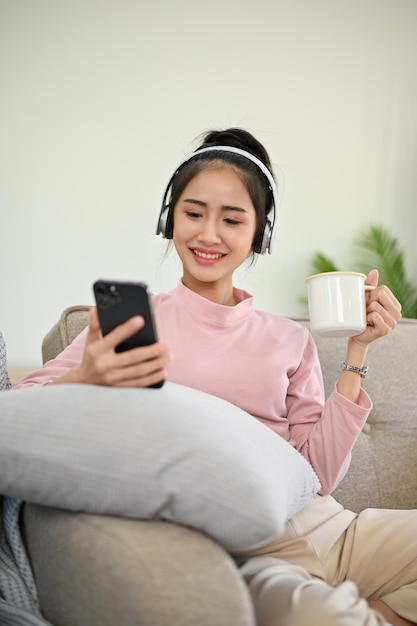 Menina asiática bonita relaxando em sua sala de estar ouvindo música através de fones de ouvido