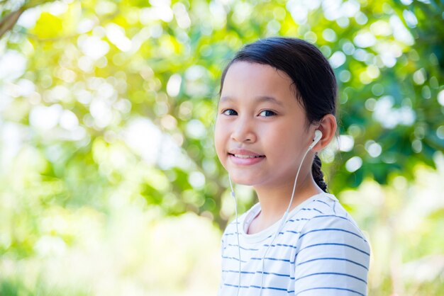 Menina asiática bonita usando fone de ouvido e sorrisos no parque