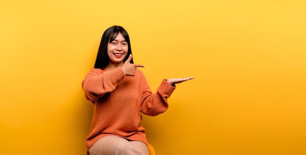 Menina asiática bonita usando um vestido laranja casual. fundo amarelo Comemore a vitória com um sorriso feliz e a expressão do vencedor com a mão levantada. expressão feliz