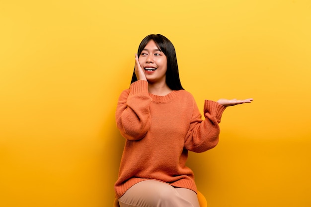 Menina asiática bonita vestindo um vestido casual laranja fundo amarelo Comemore a vitória com um sorriso feliz e a expressão do vencedor com uma expressão feliz de mão levantada