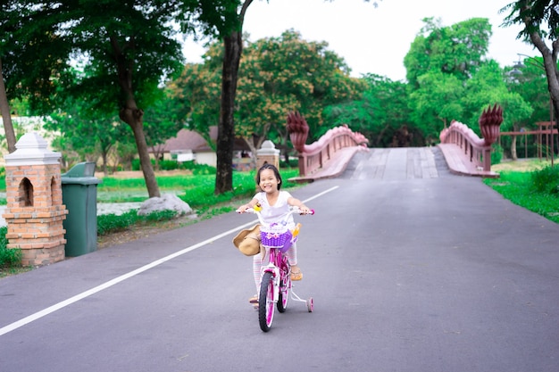 Menina asiática bonitinha andando de bicicleta para se exercitar no parque, esportes infantis e estilo de vida ativo