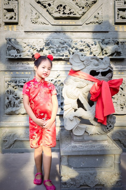 Menina asiática bonitinha em vestido tradicional chinês, sorrindo e em pé perto da estátua.