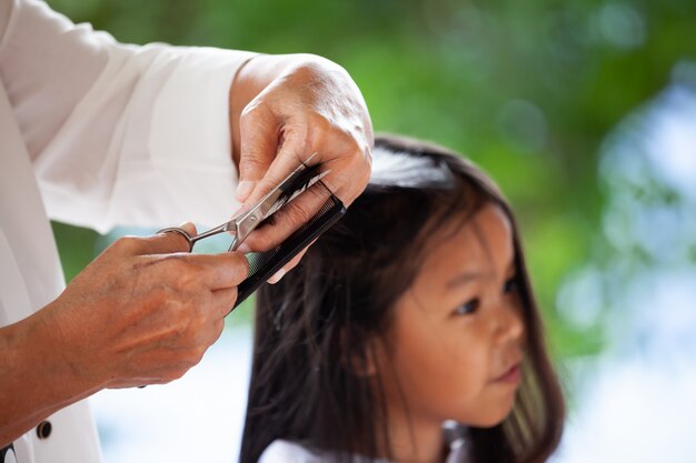 Menina asiática bonito da criança que corta o cabelo pela avó em casa