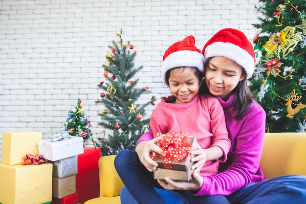 menina asiática com a mãe dela segurando a caixa de presente bonita e surpresa com presente na celebração de Natal