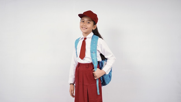 Foto menina asiática com chapéu e bolsa escolar sorrindo alegremente no fundo branco isolado