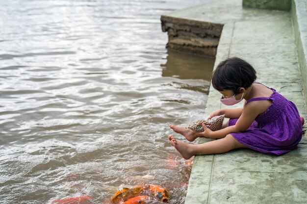 Menina asiática com máscara facial saudável sentada no lago