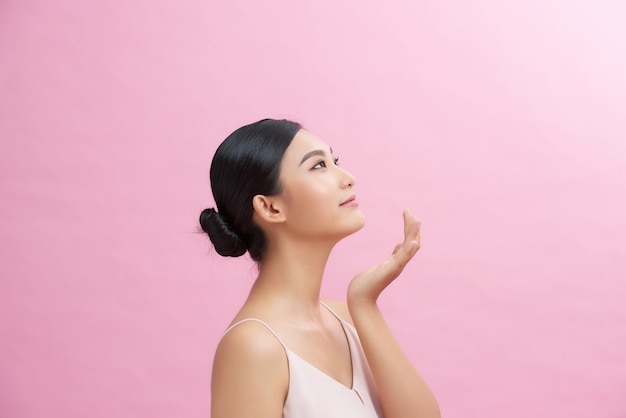 Menina asiática com pele brilhante perfeita e maquiagem natural nude posando contra um fundo rosa.