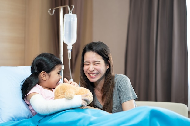 Menina asiática com um braço quebrado usando gesso na cama do hospital com a mãe