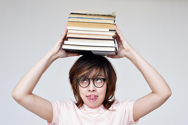 Menina asiática com uma pilha de livros na cabeça obter educação ou hobby lendo livros