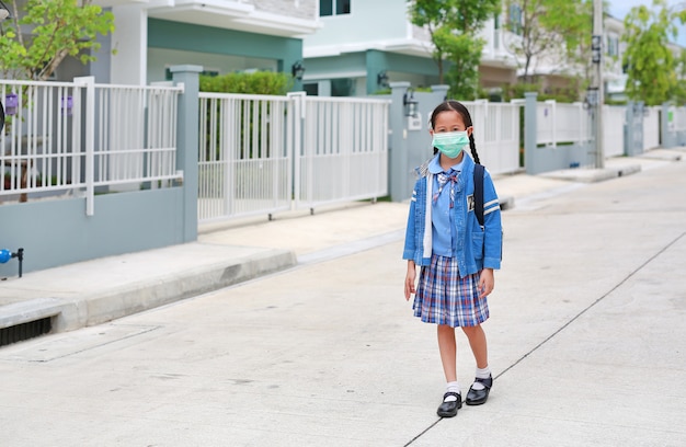 Menina asiática com uniforme escolar e máscara médica andando na rua