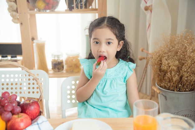 Menina asiática comendo morango na mesa de café da manhã