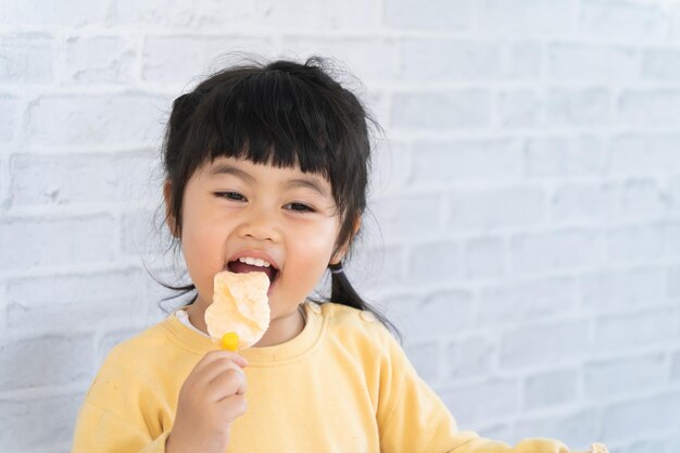 Menina asiática comendo sorvete em fundo cinza. Conceito de estilo de vida do bebê