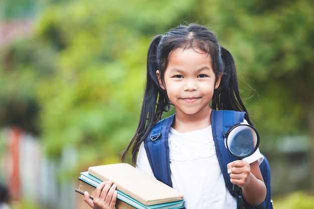 Menina asiática criança com mochila segurando livros e lupa pronto para ir à escola