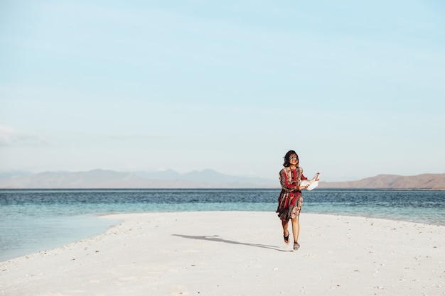 Menina asiática curtindo as férias e correndo na praia de areia branca