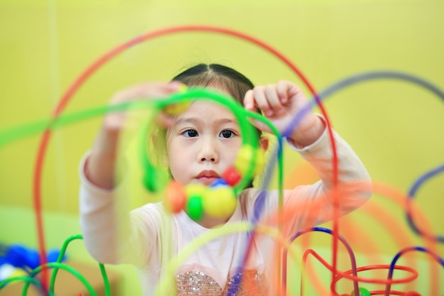 Menina asiática da criança do close-up que joga o brinquedo educacional para o desenvolvimento do cérebro na sala das crianças.
