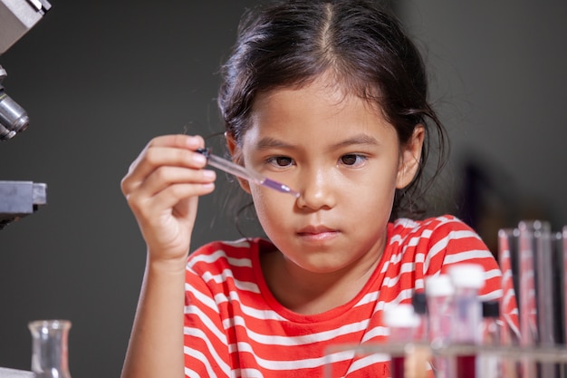 Menina asiática da criança que faz a experiência química no laboratório.