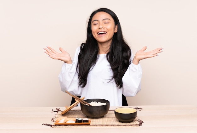 Menina asiática de adolescente comendo comida asiática na parede bege sorrindo muito