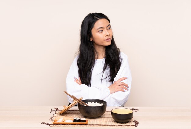 Menina asiática de adolescente comendo comida asiática na parede bege