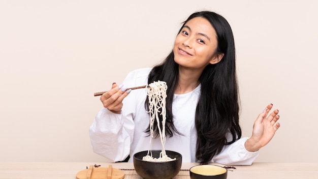 Menina asiática de adolescente comendo comida asiática na parede bege