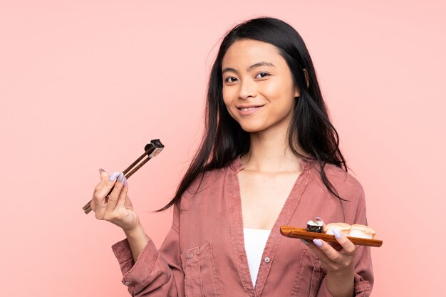 Menina asiática de adolescente comendo sushi na parede rosa