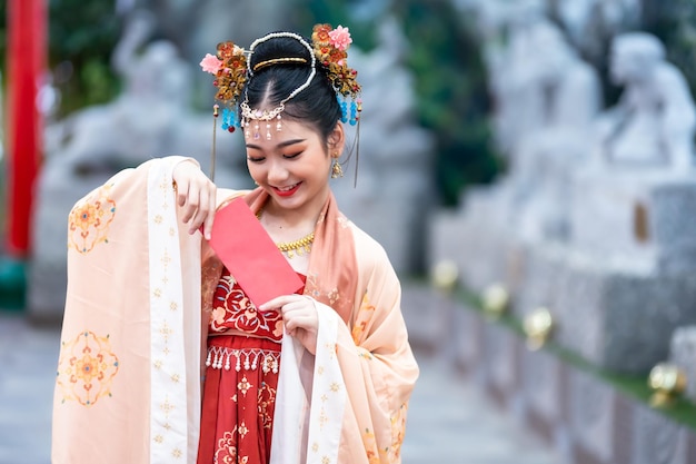 Menina asiática de beleza feliz vestindo trajes antigos chineses segurando a decoração de envelopes vermelhos para o festival do ano novo chinês celebra a cultura da china no santuário chinês Lugares públicos na Tailândia