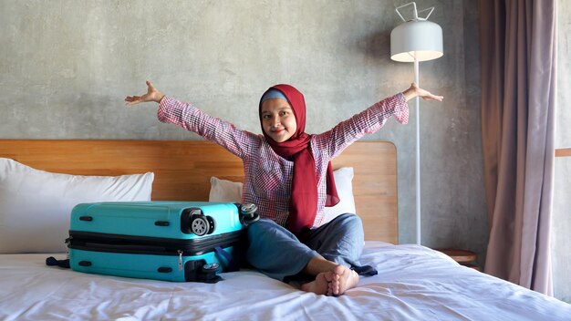 Menina asiática de hijab feliz no quarto com uma mala porque quer viajar
