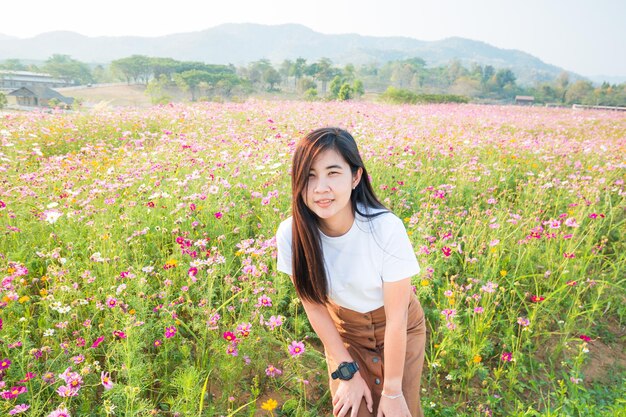 Menina asiática de vestido branco sentada em um prado de flores cor de rosa no campo