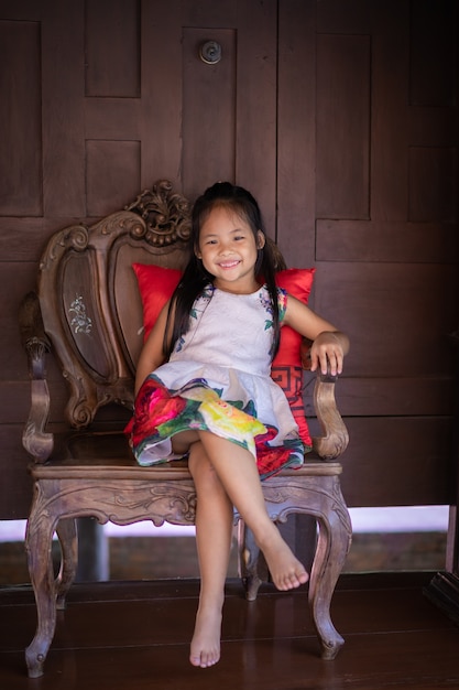 Menina asiática de vestido sentada na cadeira em casa