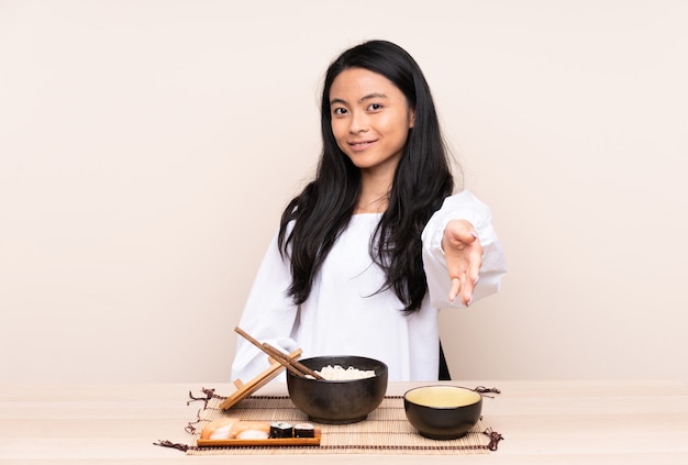 Menina asiática do adolescente que come a comida asiática isolada no bege