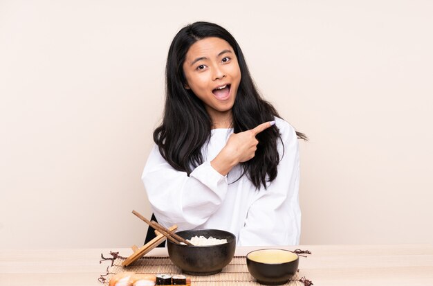 Menina asiática do adolescente que come a comida asiática isolada no bege