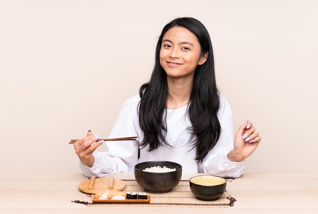 Menina asiática do adolescente que come a comida asiática isolada no bege