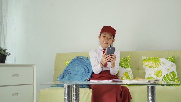 Menina asiática do ensino fundamental em busca de ideias em seu smartphone para material de estudo em casa
