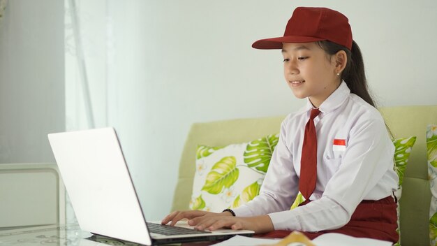 Menina asiática do ensino fundamental estudando on-line em casa digitando no laptop