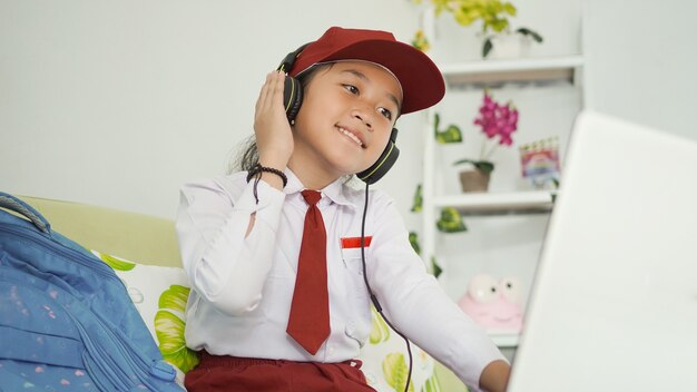 Menina asiática do ensino fundamental estudando online em casa e ouvindo com fone de ouvido